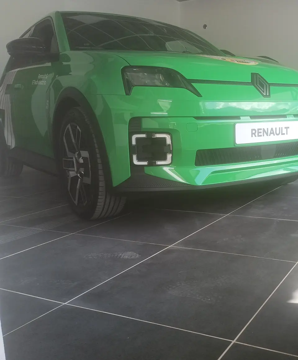 Le hall d’exposition du garage : une Renault 5 neuve sur le carrelage gris.